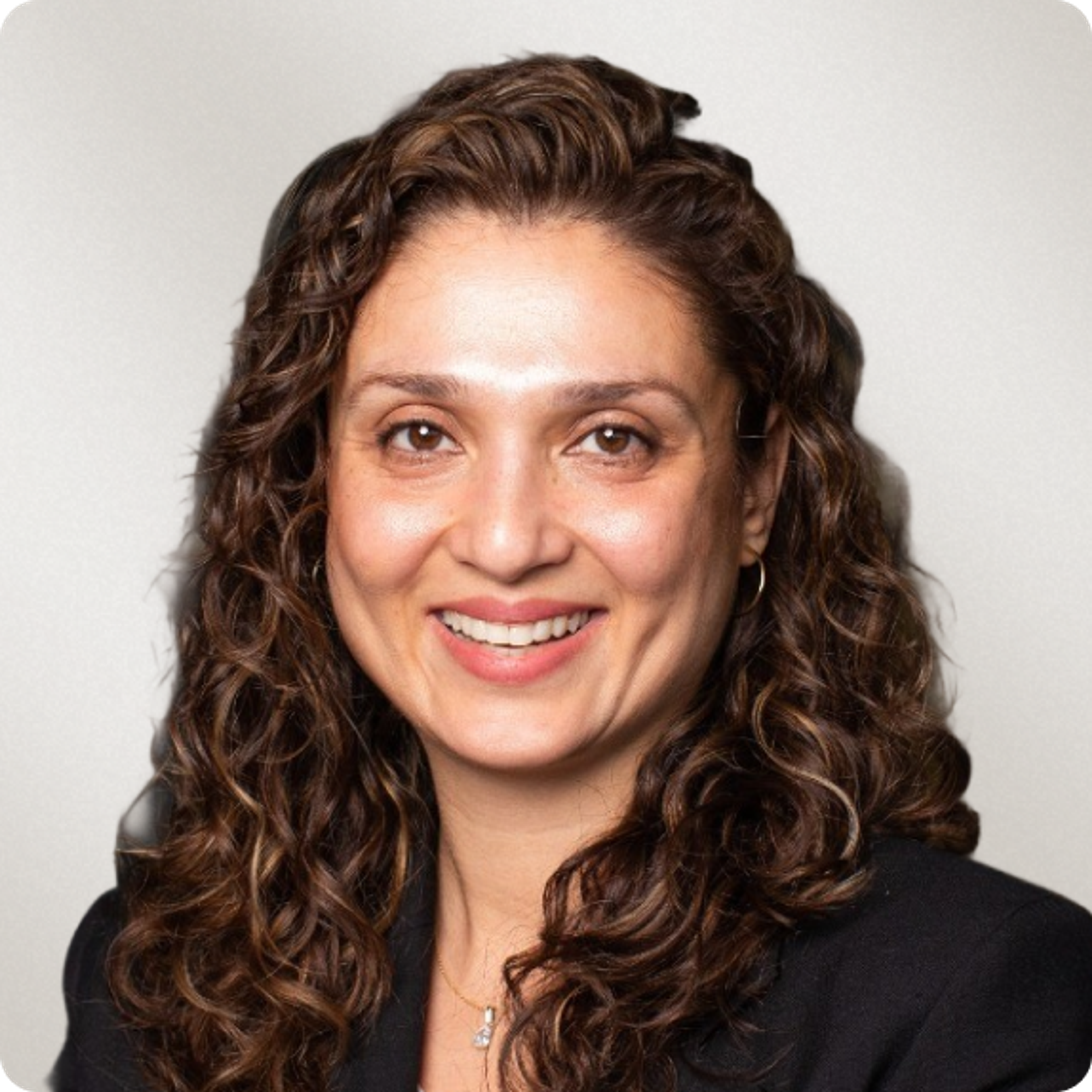 A smiling woman with long curly brown hair, wearing a black blazer and a necklace.