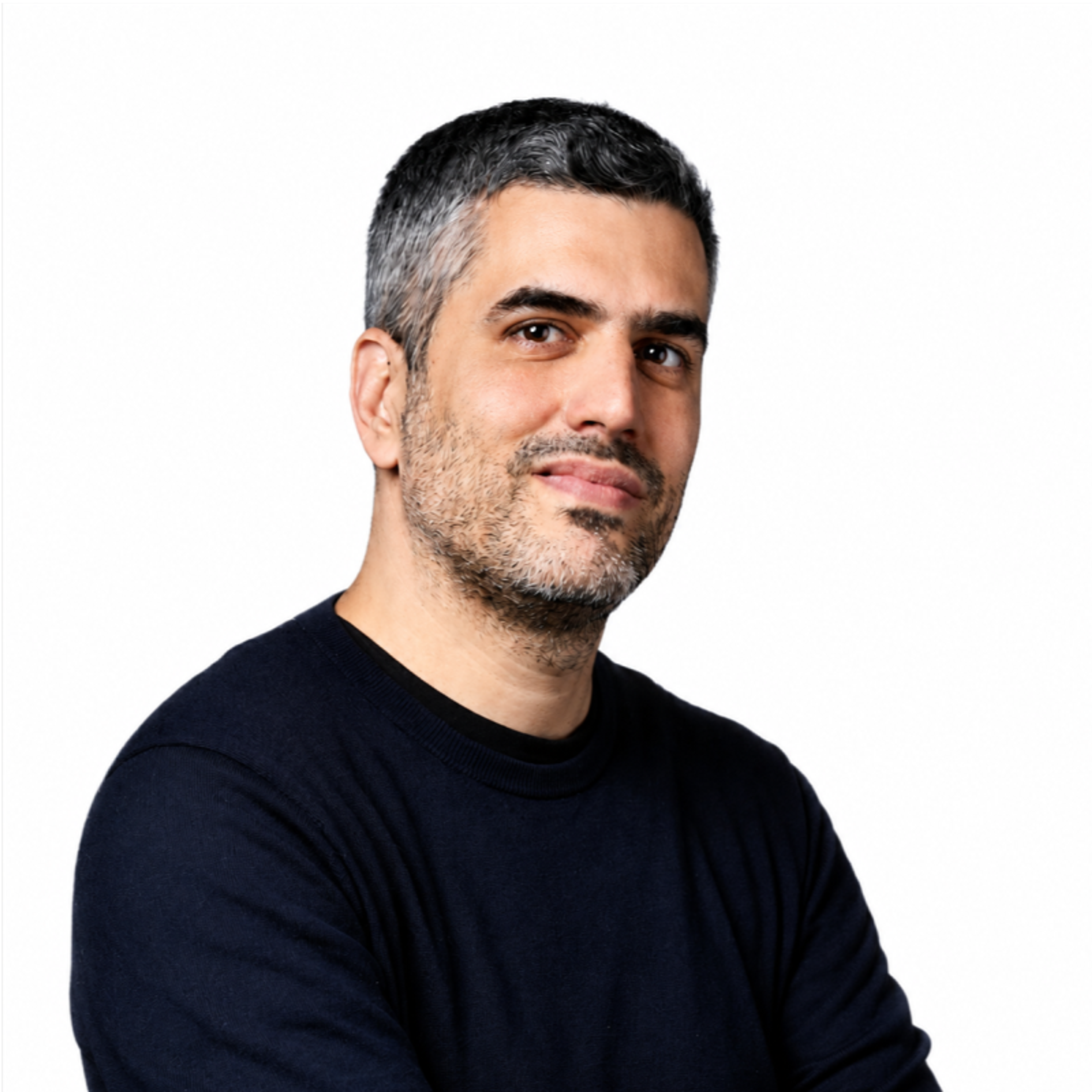 A man with salt-and-pepper hair and a beard, wearing a dark sweater, smiles gently against a white background.