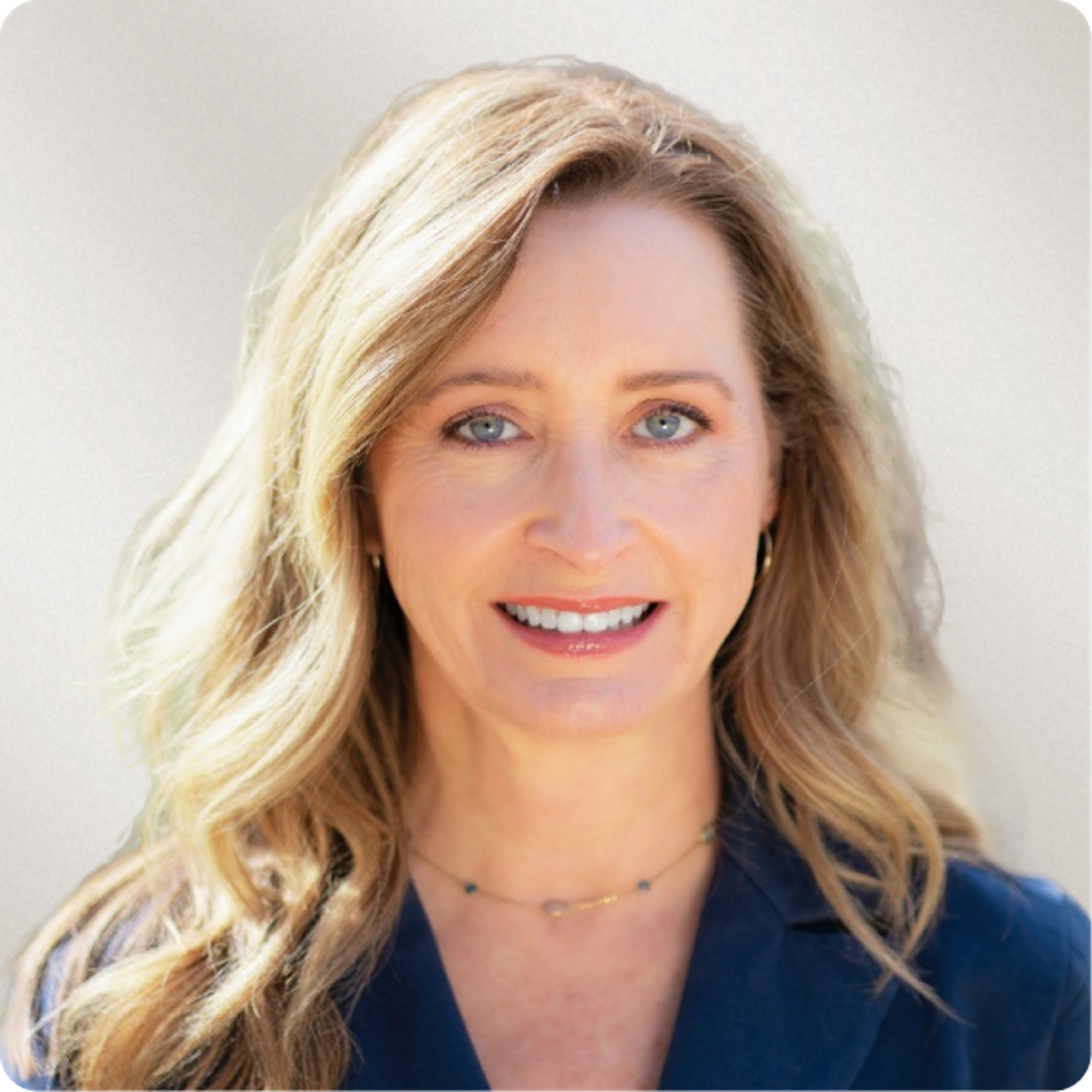 Headshot of a smiling woman with blonde hair, blue eyes, and a navy blue jacket.
