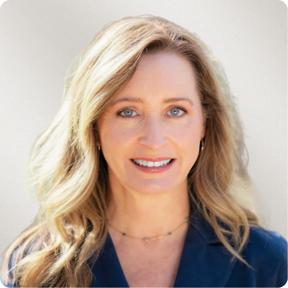 Headshot of a smiling woman with blonde hair, blue eyes, and a navy blue jacket.