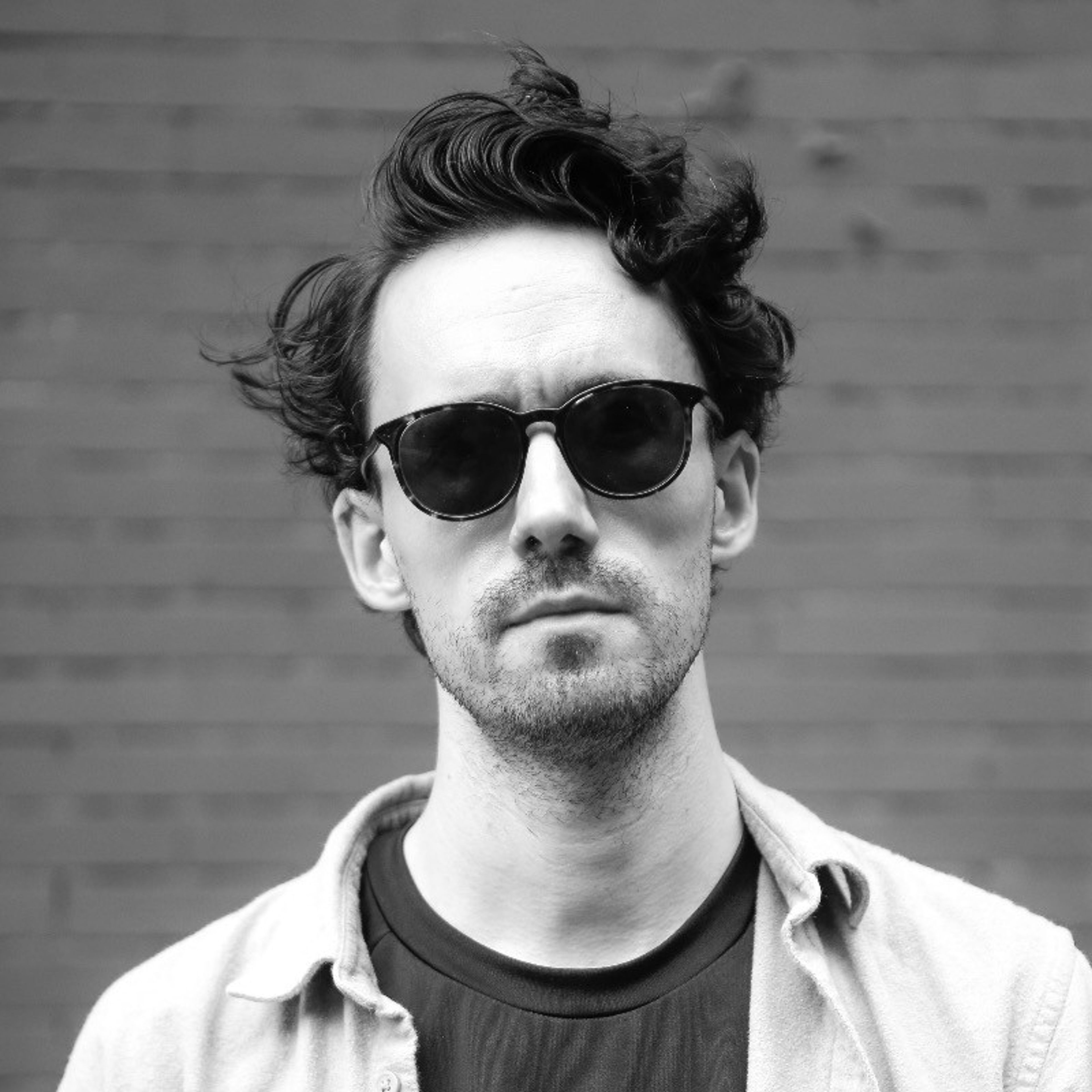 Black and white photo of a man with messy curly hair, sunglasses, and a beard.