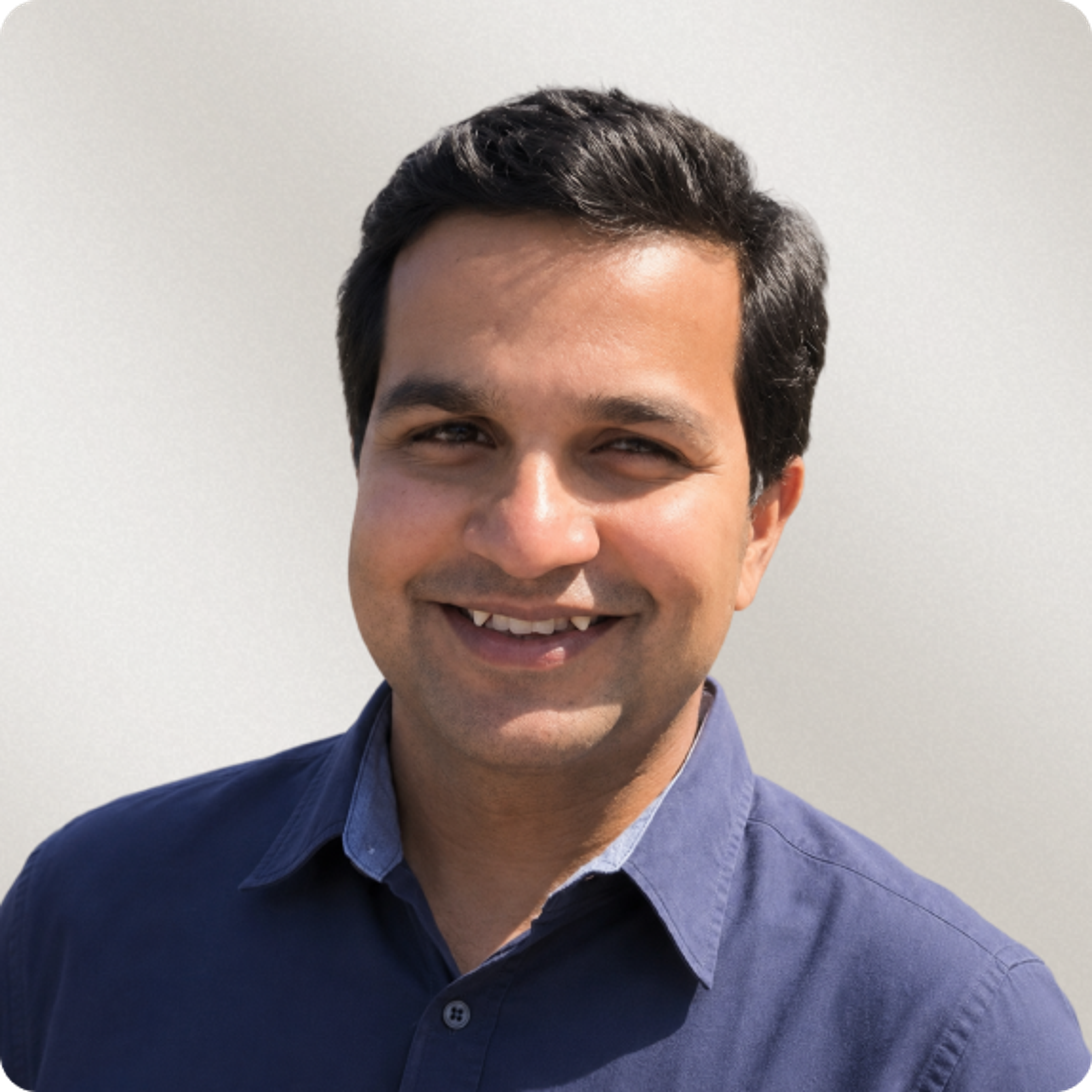 Smiling man with dark hair in a blue shirt.