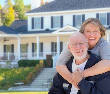 Senior couple standing in front of new house.