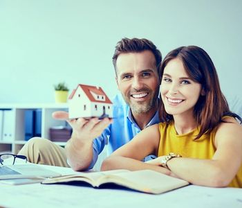 Couple holding house model and reading documents.