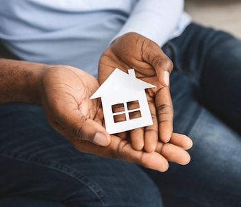 Hands holding a small house model.