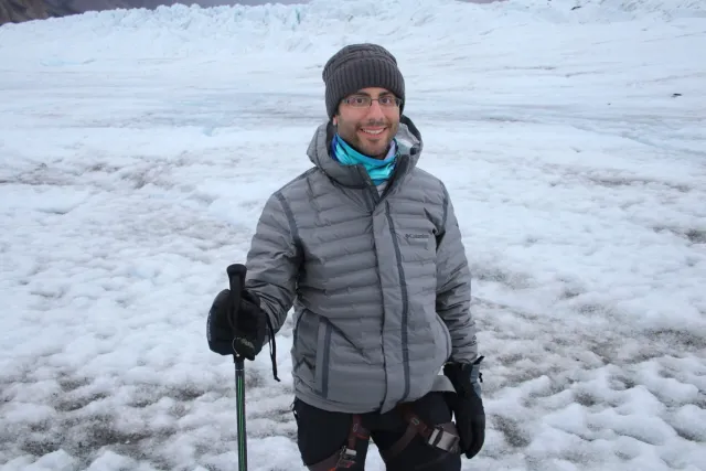 A hiker standing on the glacier and holding an ice axe.