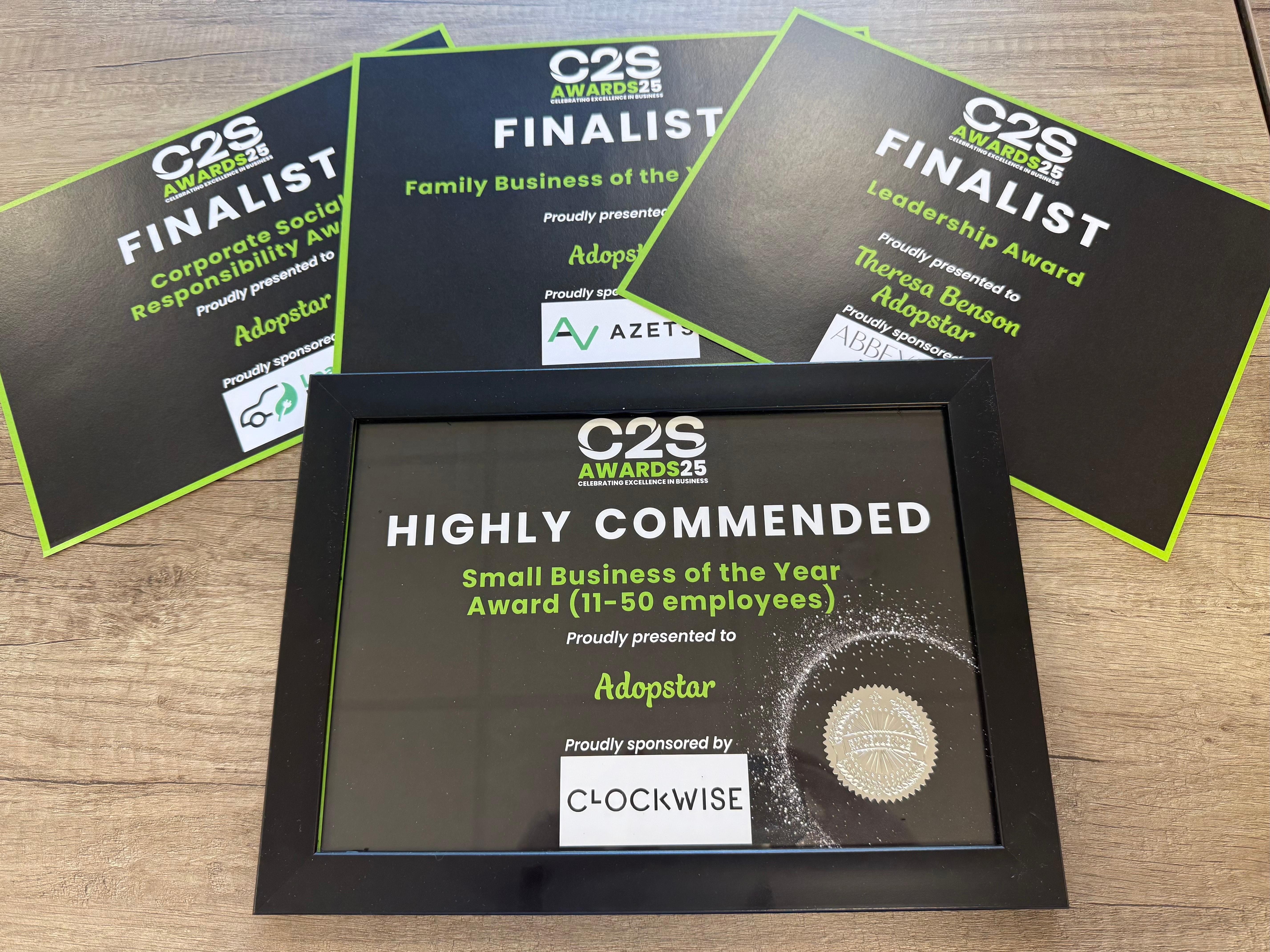 Multiple black and green award certificates and a framed 'Highly Commended' award, all from C2S Awards 25, recognising 'Adopstar' as a finalist in categories like Corporate Social Responsibility, Family Business, and Leadership Award, and highly commended for Small Business of the Year.
