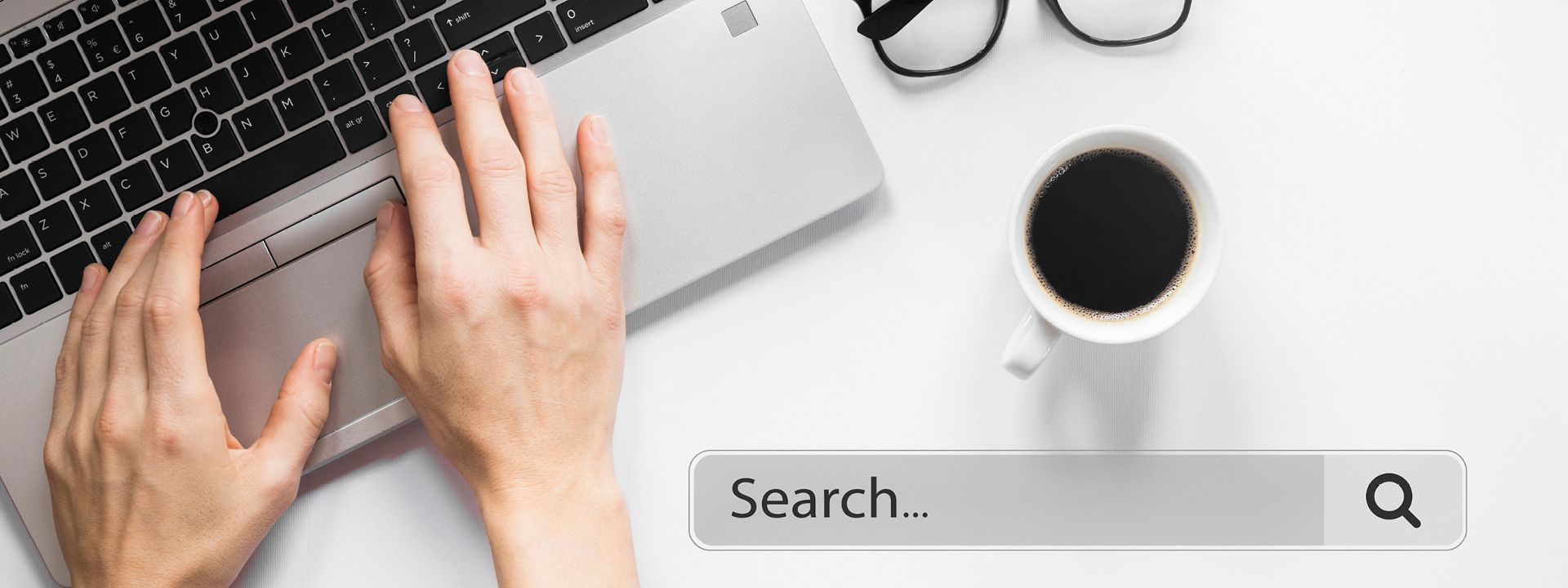 A top-down view shows hands typing on a laptop keyboard next to a white coffee mug and a pair of glasses, with a search bar prominent in the foreground, representing blog writing or content creation.