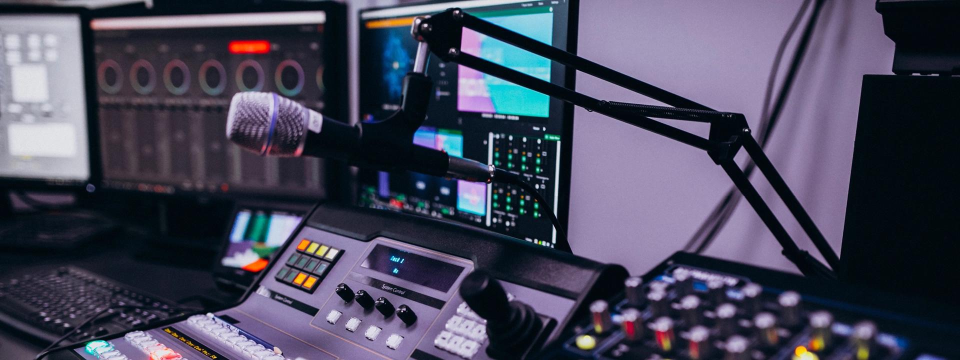  Microphone in a radio studio with sound mixing equipment and computer monitors in the background showcasing Radio Advertising.