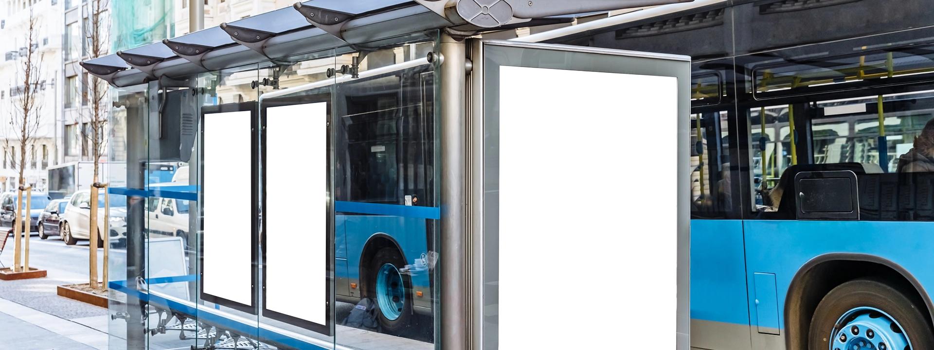 Three blank white advertising panels are visible within a modern bus stop shelter, with a blue city bus parked alongside, illustrating out-of-home advertising opportunities.