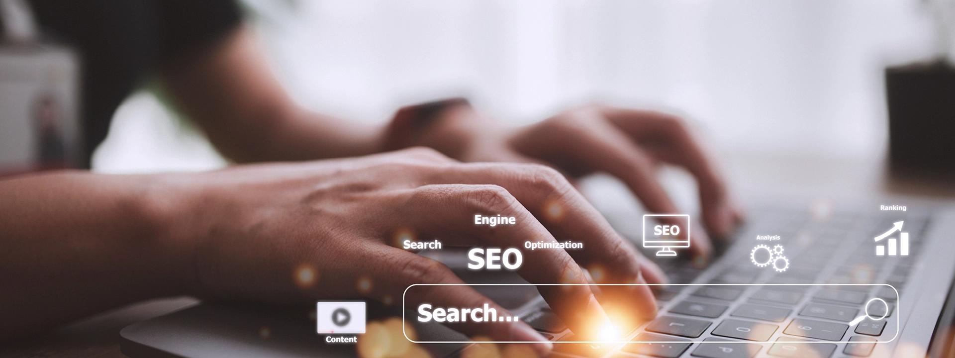 Hands are typing on a laptop keyboard, with a glowing search bar and various floating digital icons and words related to SEO, including "SEO," "Search," "Engine," "Optimisation," "Analysis," and a rising bar graph, symbolising enterprise SEO.