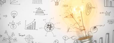 A bright, illuminated lightbulb is positioned over a white surface covered with various hand-drawn business and mathematical diagrams, charts, and equations, suggesting concepts like ideas, planning, analysis, and growth.