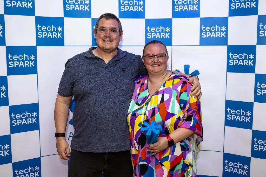 Man and woman holding an award in front of a "tech*SPARK" logo backdrop. Winner of Best Place To Work in Tech at The SPARKies 2024.