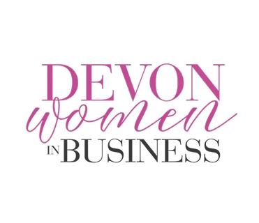 The image displays the logo for "Devon Women in Business". "DEVON" is in large, bold magenta uppercase letters. Below it, "women" is in a magenta script font. "IN" is in smaller, black uppercase letters, and "BUSINESS" is in large, black uppercase letters, both sans-serif. The background is white.
