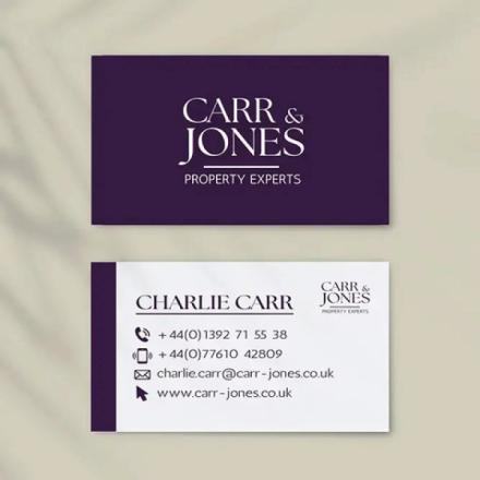  Two "CARR & JONES PROPERTY EXPERTS" business cards are displayed. The top card is dark purple with white text, showing only the logo. The bottom card is white with a purple stripe on the left, featuring "CHARLIE CARR" in bold, contact details including phone, email, and website, and a smaller version of the company logo.