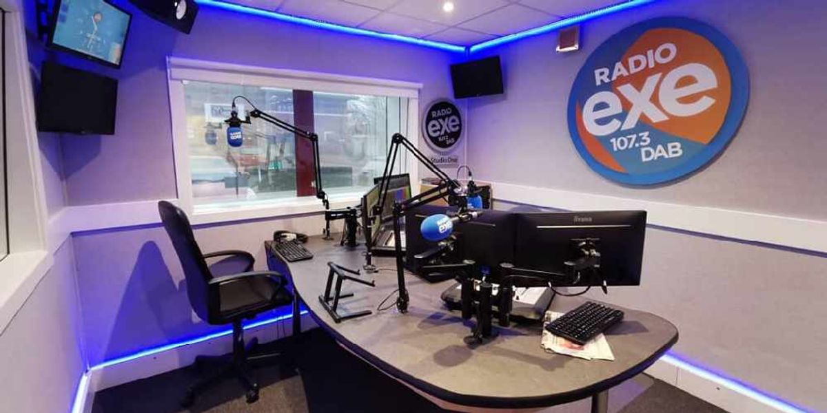 Radio Exe Exeter broadcast studio with curved desk, boom microphones and branded monitors