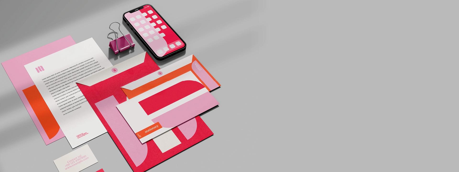 A vibrant corporate branding mockup with a smartphone, letterhead, and envelopes in a coordinated pink and red colour scheme, representing professional identity."