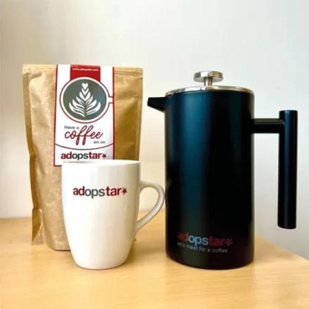  A brown bag of "adopstar" coffee beans, a white mug with the "adopstar" logo, and a black French press are arranged on a wooden surface.