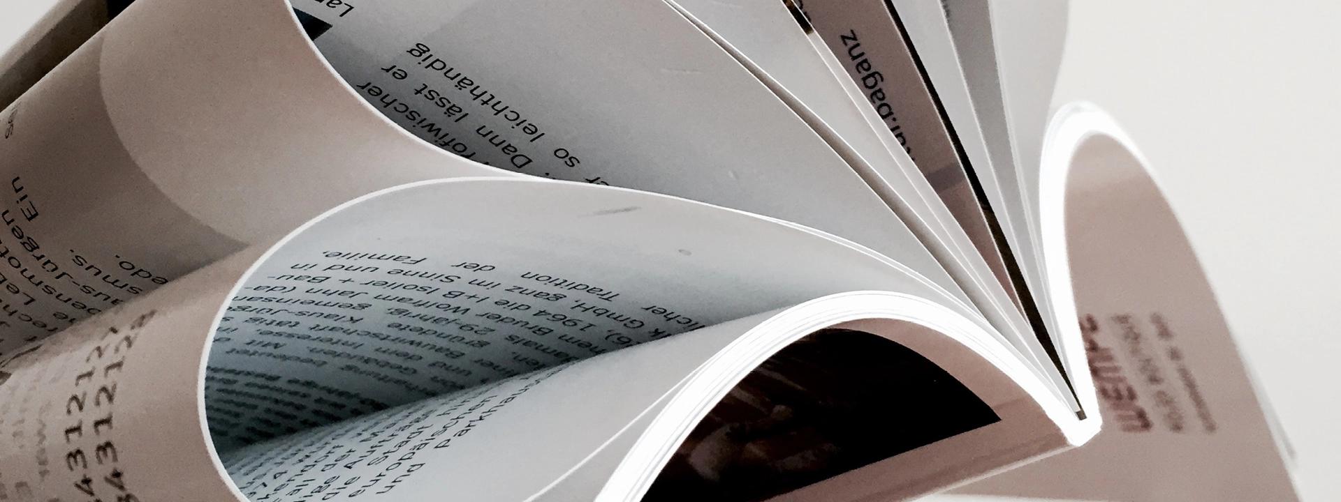 "A close-up, artistic shot of the fanned-out pages of a magazine or publication, showcasing the texture of the paper and printed text symbolising editorial & publication design