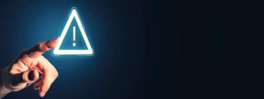  A hand is pointing towards a glowing white outlined triangle with an exclamation mark inside, set against a dark blue background with ample copy space to the right.