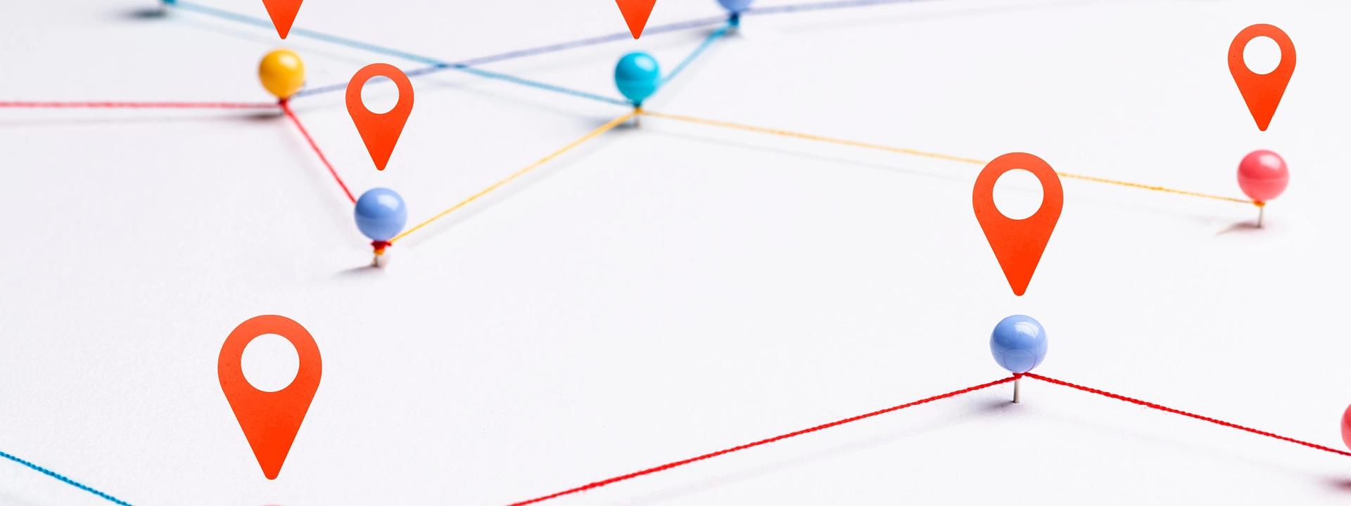A white surface with colorful pushpins connected by red and blue strings, with several prominent orange location pin icons overlaid, illustrating interconnected points or a customer journey map.