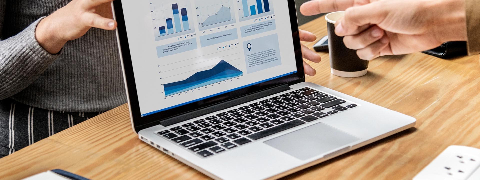 Two people are reviewing data on a laptop screen that displays various charts and graphs, including bar charts and line graphs, suggesting an SEO audit or data analysis in progress.