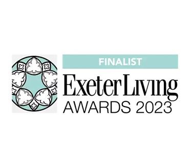 The image is a clean, white graphic displaying the "Exeter Living Awards 2023 FINALIST" logo. To the left is a circular emblem with a teal background and a white patterned design. To the right, "FINALIST" is in white text on a teal banner, followed by "ExeterLiving" in large black serif font, and "AWARDS 2023" in smaller black text below.