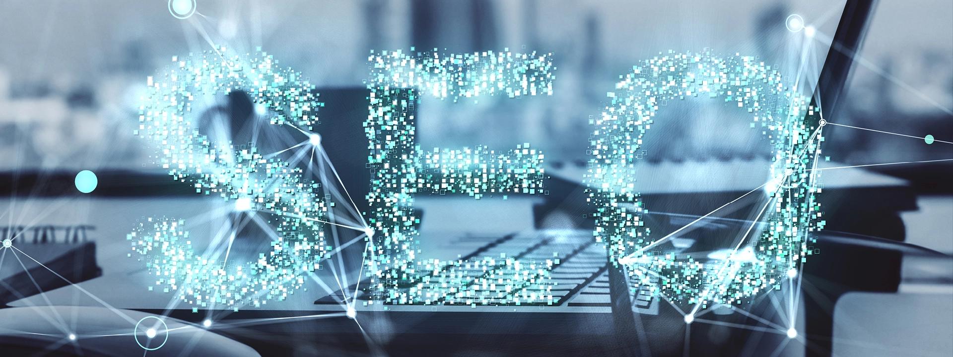 A digital representation of "SEO" made of glowing, interconnected particles, overlaid on a blurred image of a laptop keyboard, symbolising technical SEO.