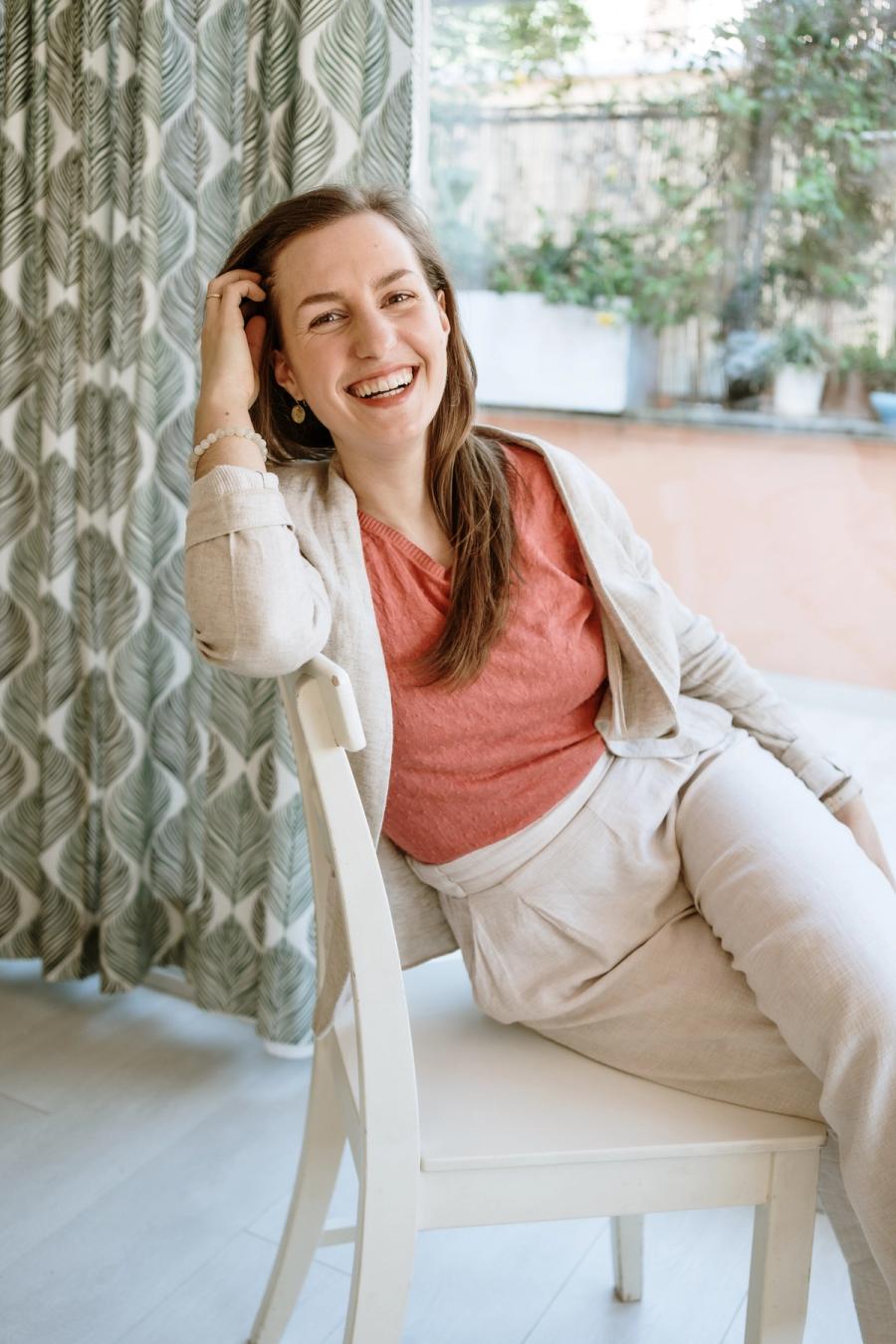 Maja Herrero sitting relaxed in a chair, smiling warmly with natural light