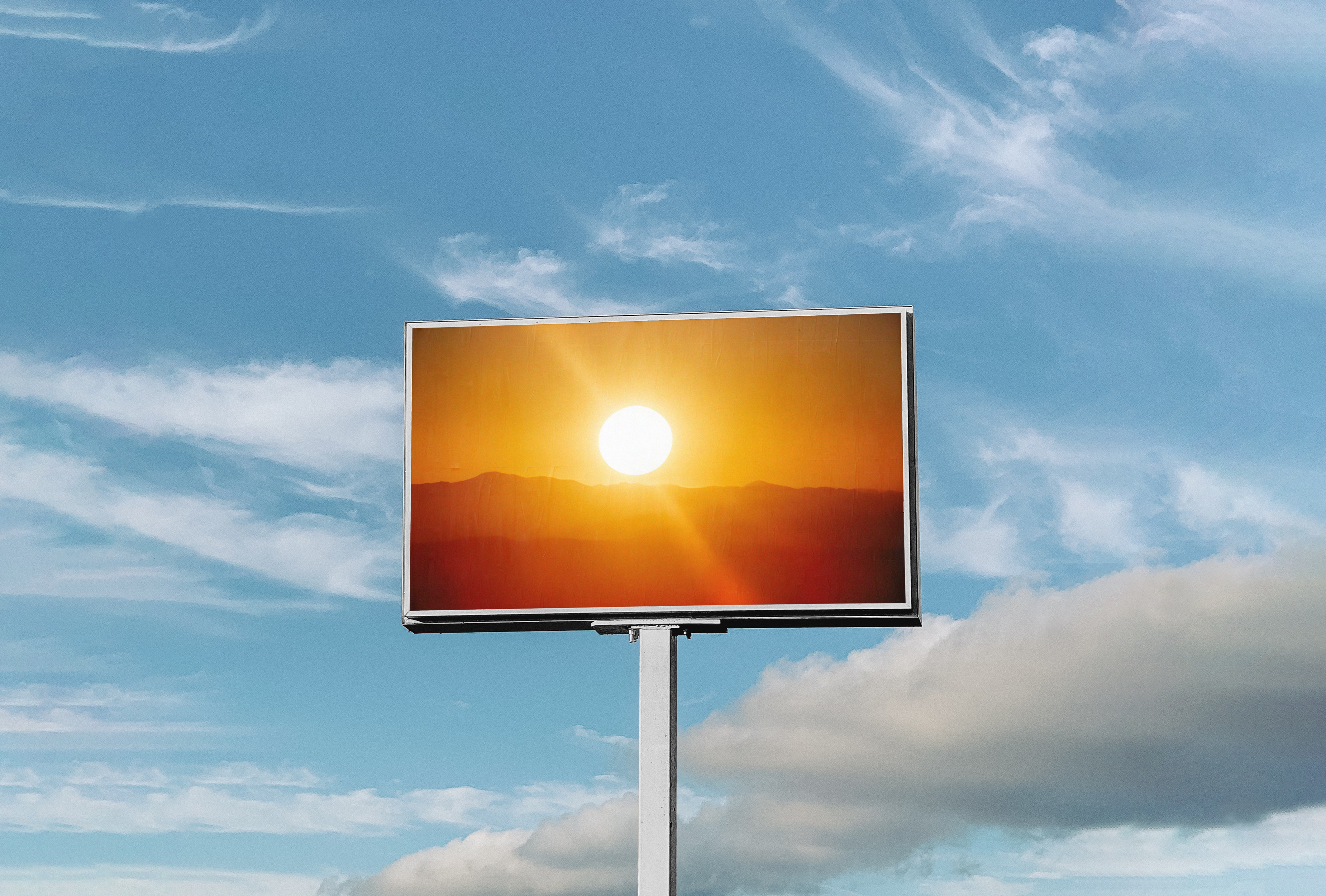 A billboard with a photo of the sunrise stands tall in a bright blue sky streaked with white clouds.
