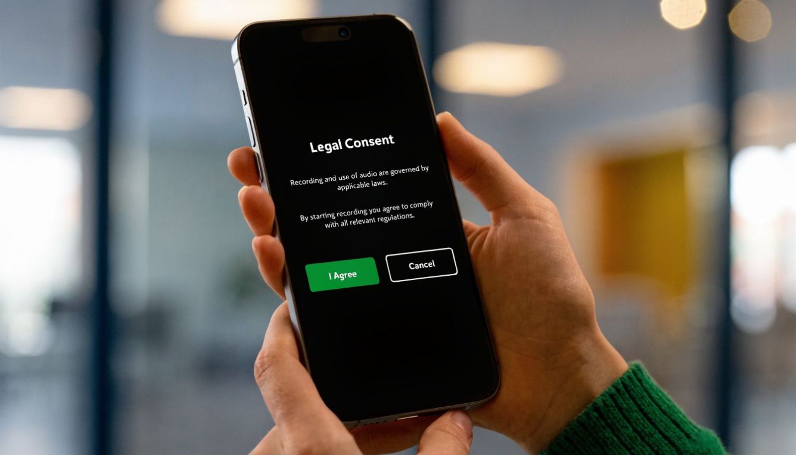 A person holding a smartphone displaying a legal consent screen for recording audio on a black background.