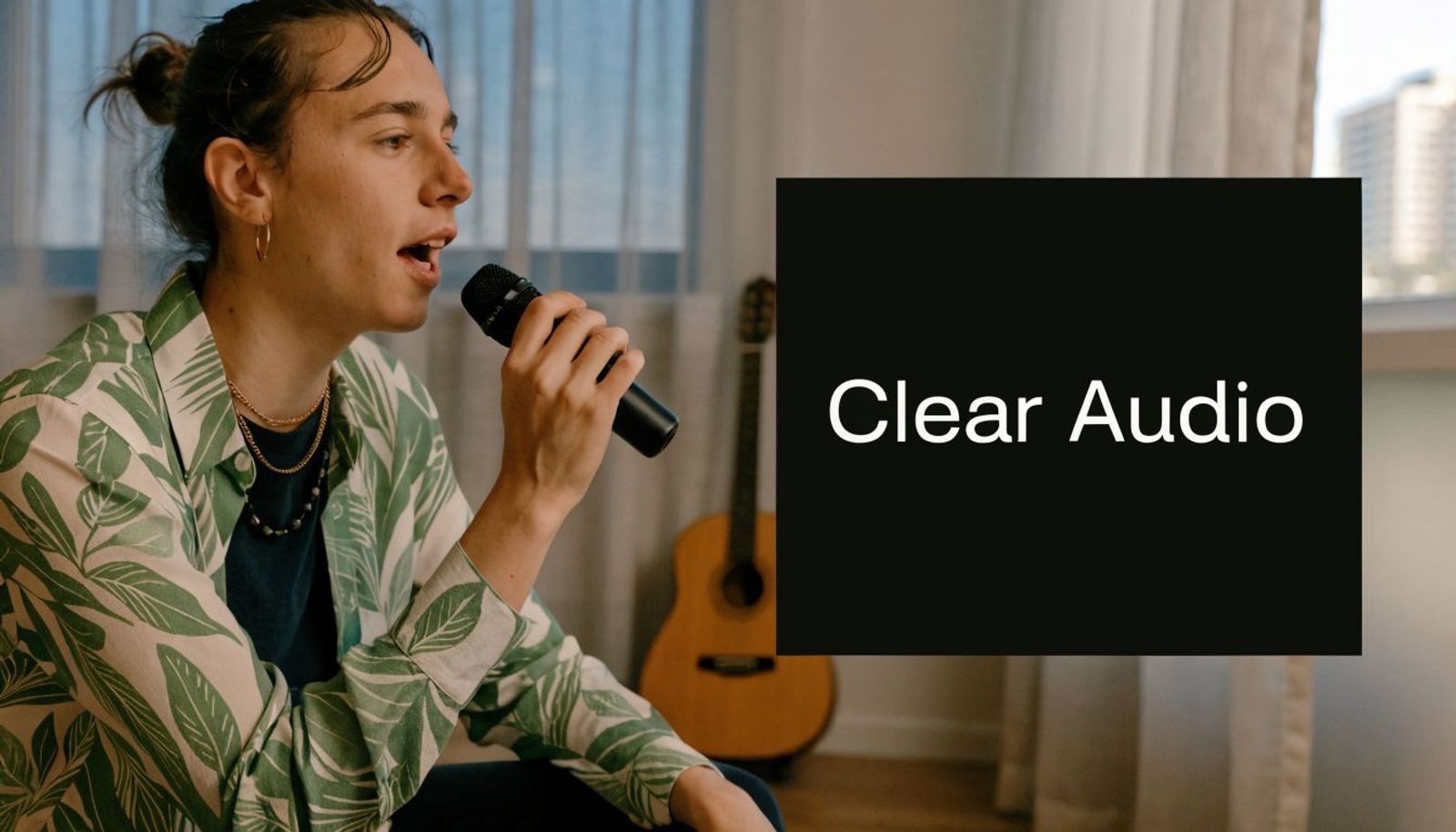 A young person singing into a microphone while holding it close in a room with a guitar.