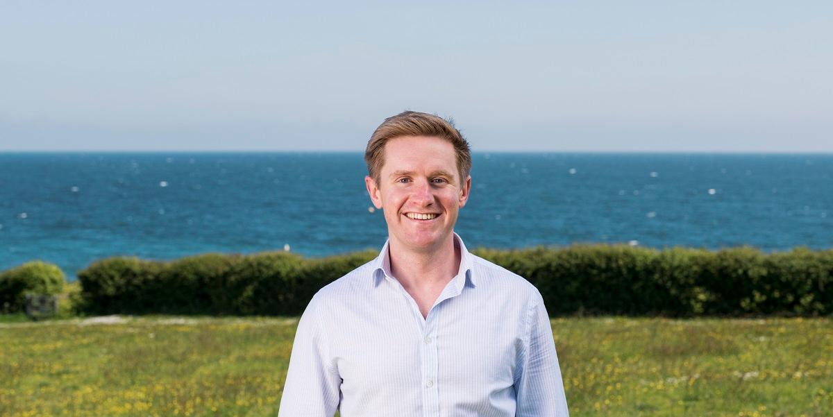 Jonty Brooks with a field, hedge and the sea in the background, Falmouth Cornwall