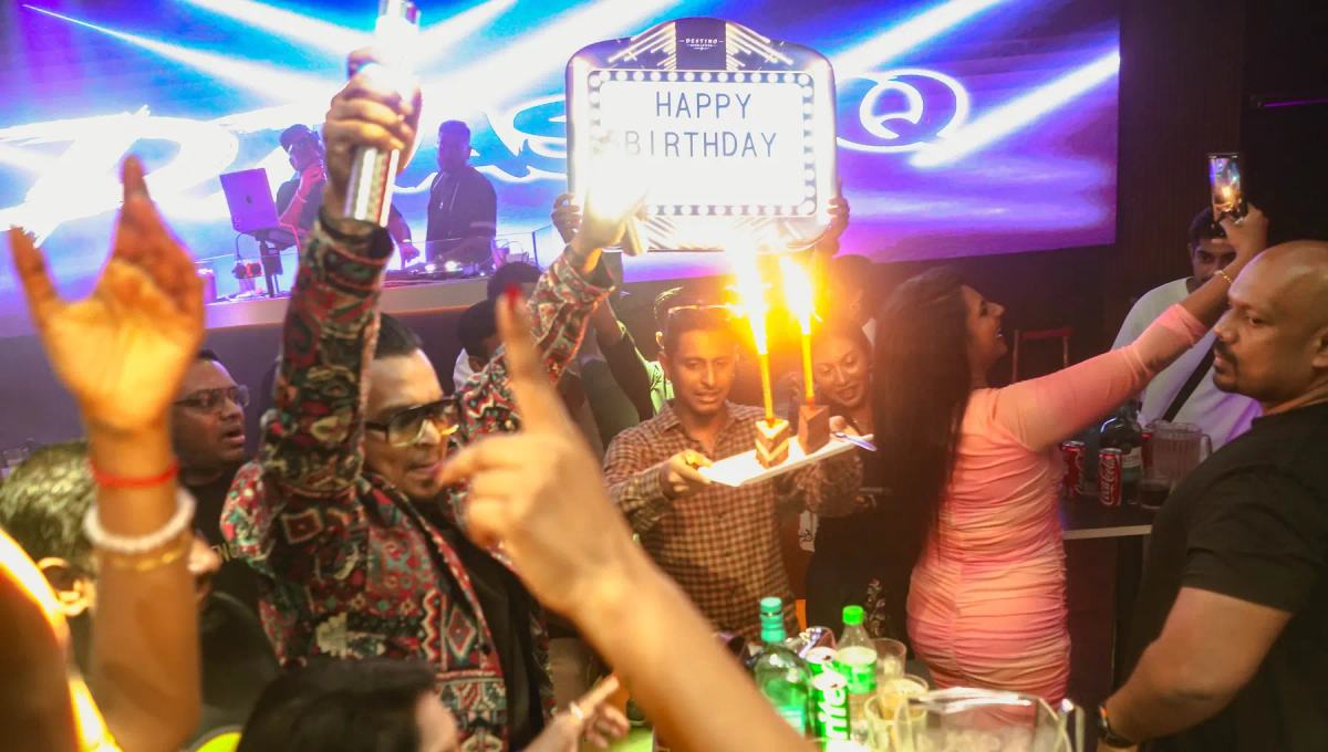 Guests cheer with hands raised around a birthday table with sparklers and a Happy Birthday sign