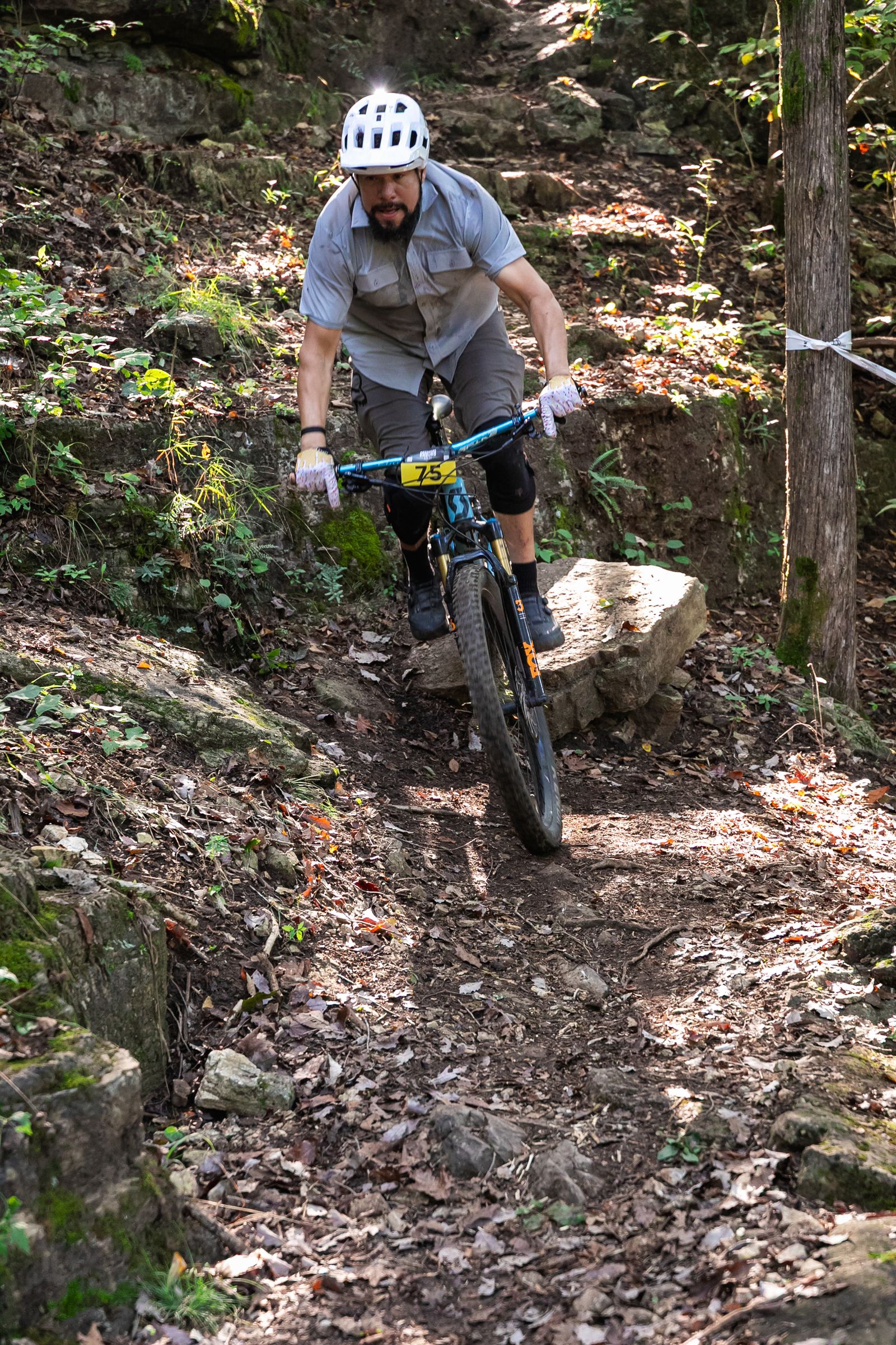 A mountain bike racer in a white helmet rides down a rocky trail