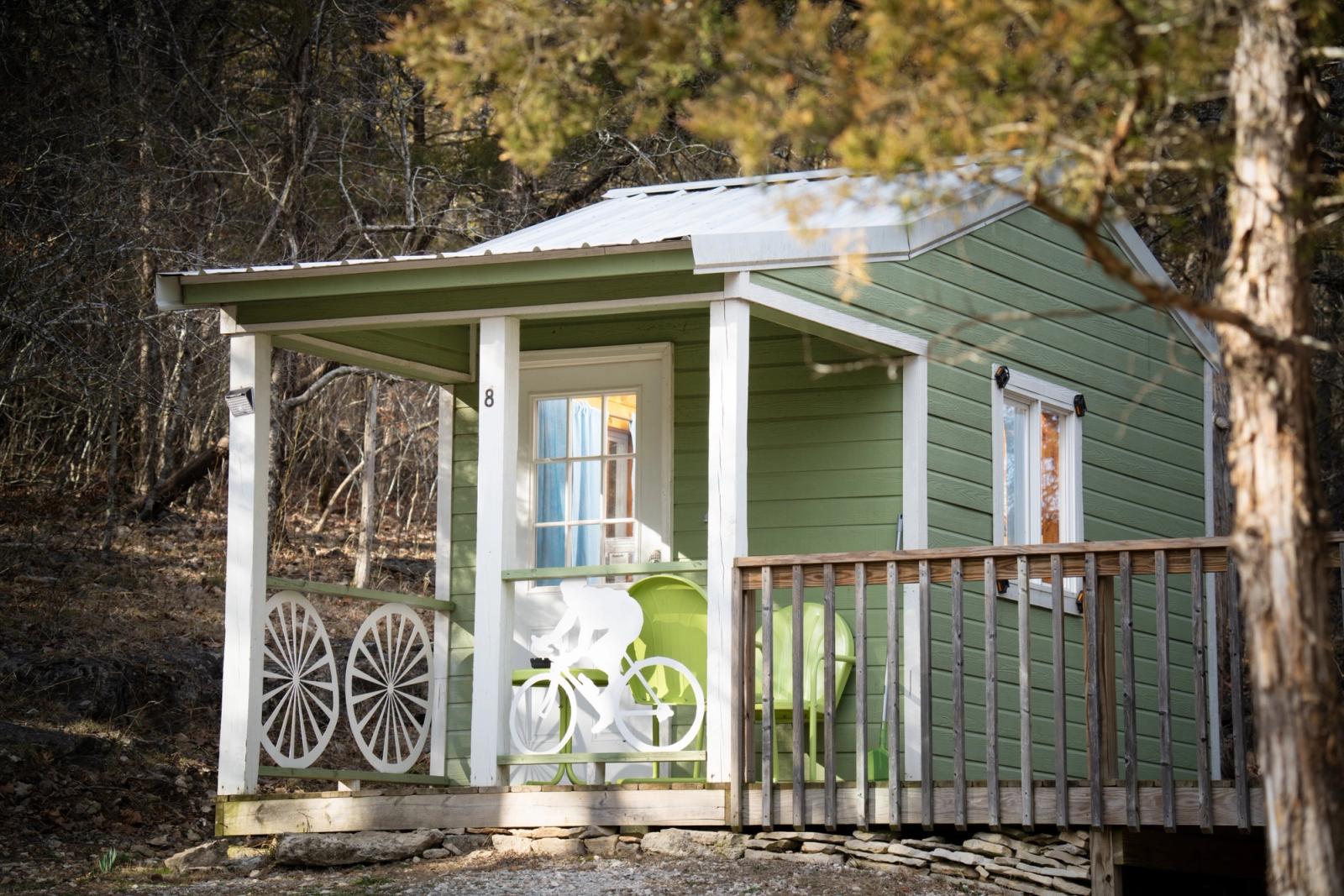 A small green mini-cabin with a front porch at Lake Leatherwood City Park