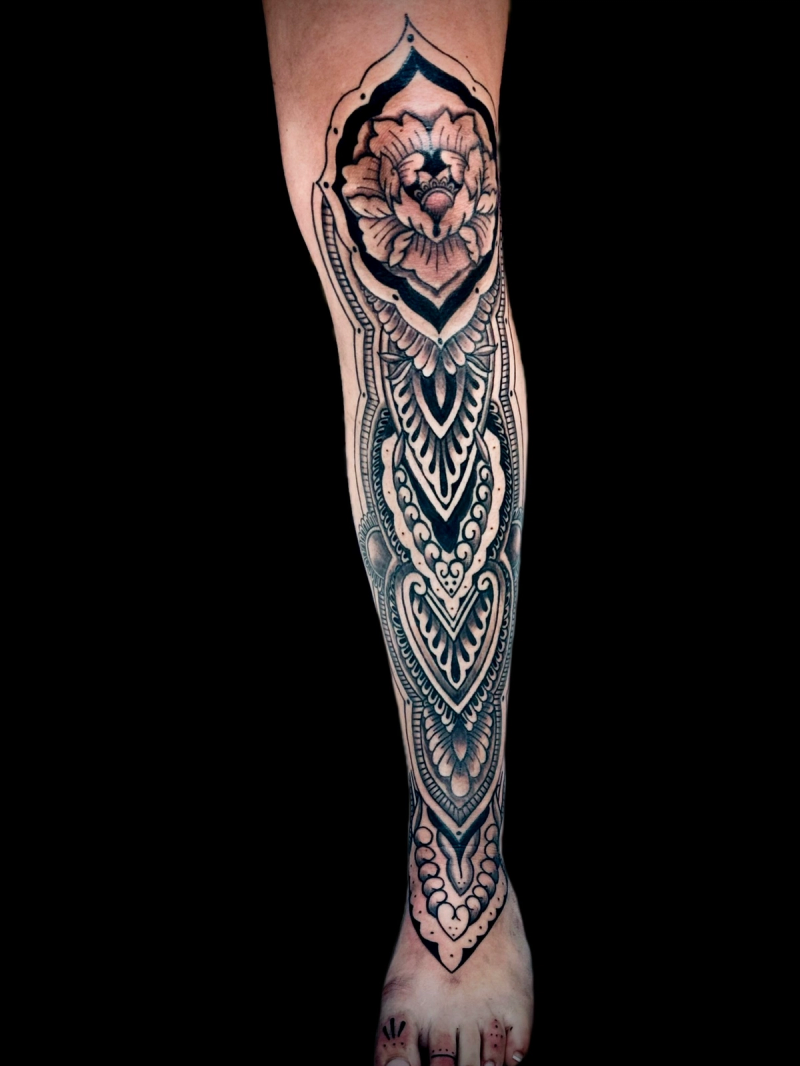 Black and grey geometric floral tattoo extending from calf to foot
