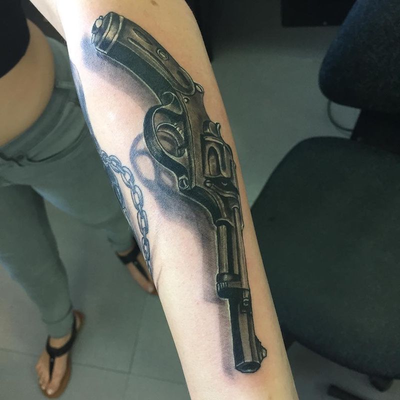 Black and grey realistic revolver tattoo on forearm