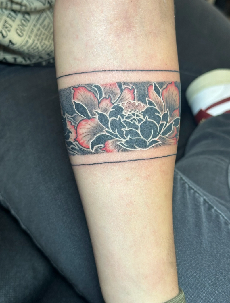Blackwork floral band tattoo with color highlights on forearm