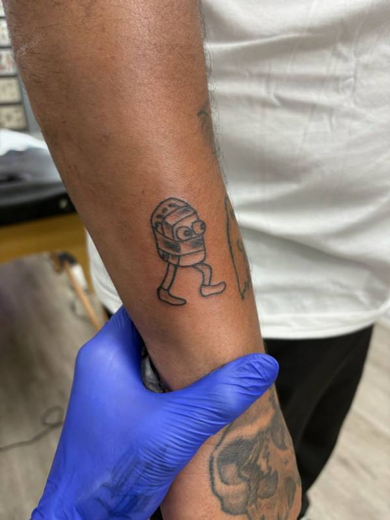 small robot character tattoo on forearm