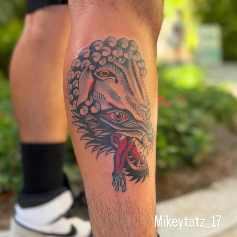 traditional style tattoo of wolf and ram heads on calf with red and blue accents