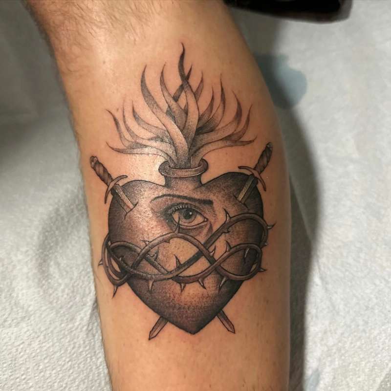 Black and grey illustrative heart with flame and eye tattoo on calf