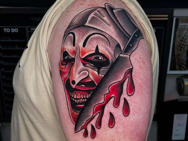 Colorful neo traditional tattoo of a clown with a knife on upper arm