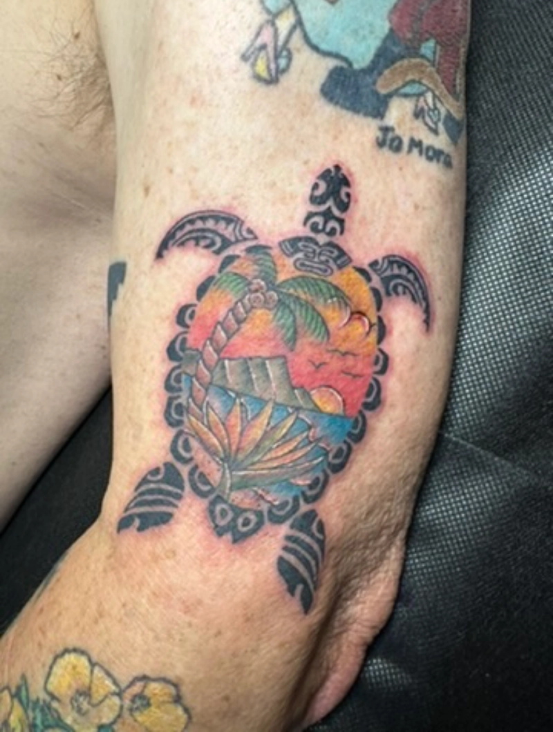 Colorful tribal turtle tattoo on forearm with sunset and palm trees.