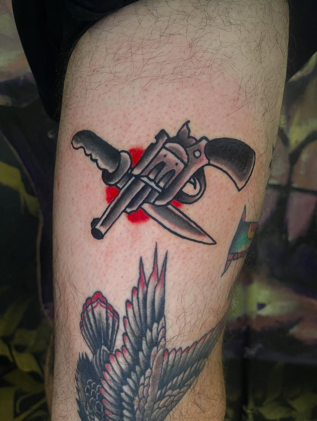 Colorful traditional revolver and knife tattoo on upper arm