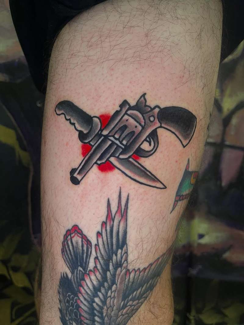 Colorful traditional revolver and knife tattoo on upper arm