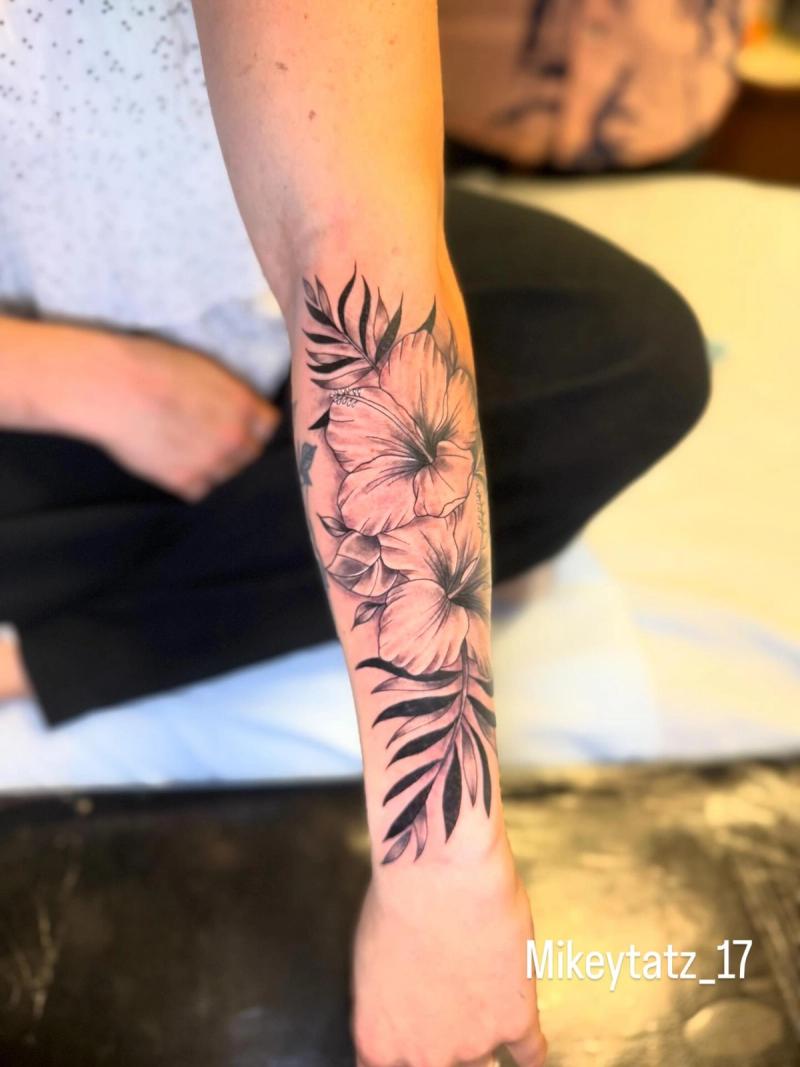 hibiscus flowers and palm leaves forearm tattoo in black and grey fine line style