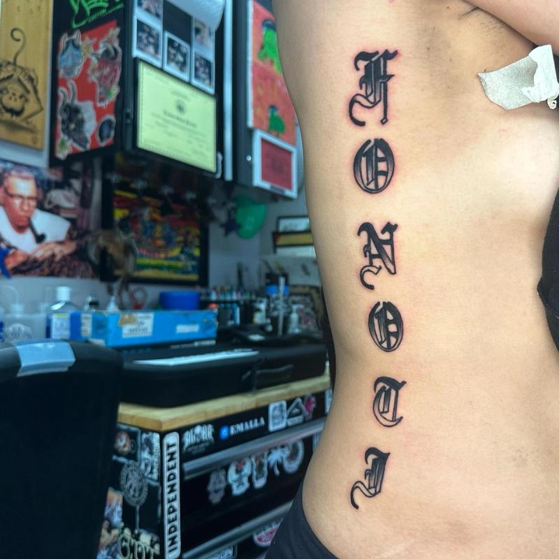 black gothic lettering tattoo on the torso
