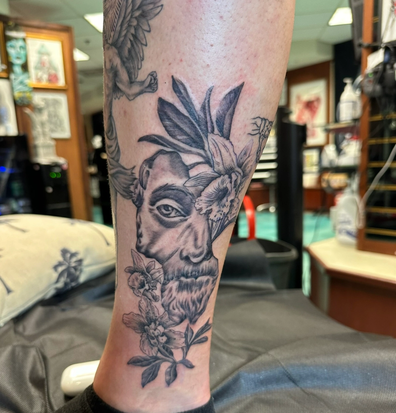 Black and grey floral intertwined face tattoo on calf