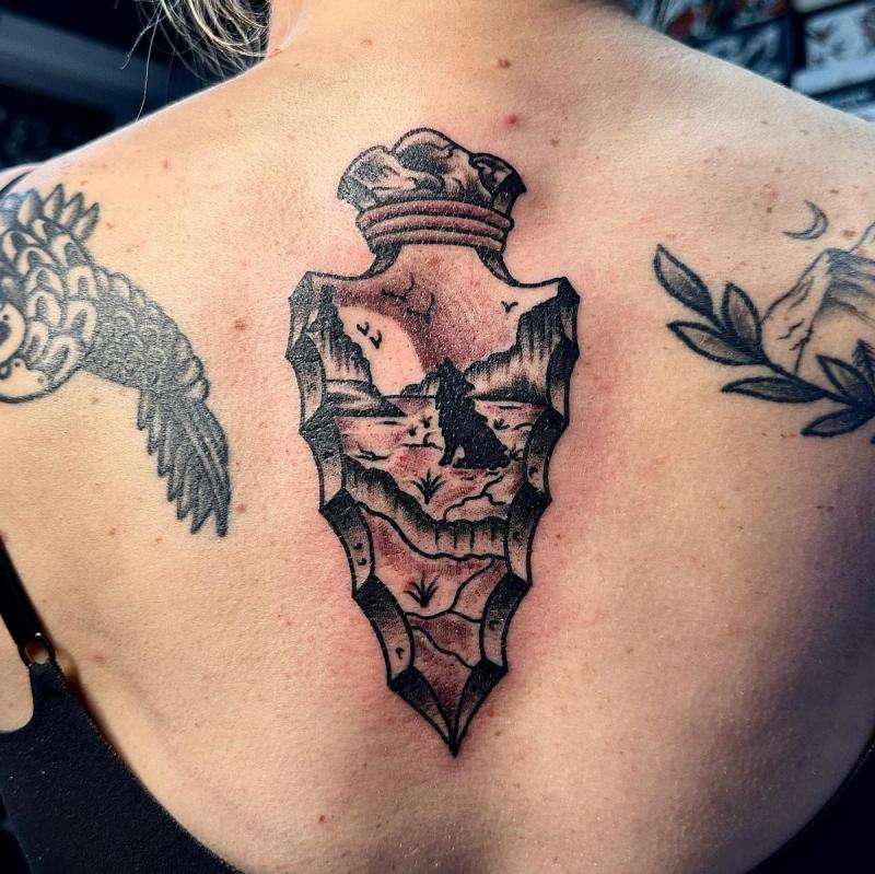 blackwork tattoo of a landscape scene in a bottle shape on upper back